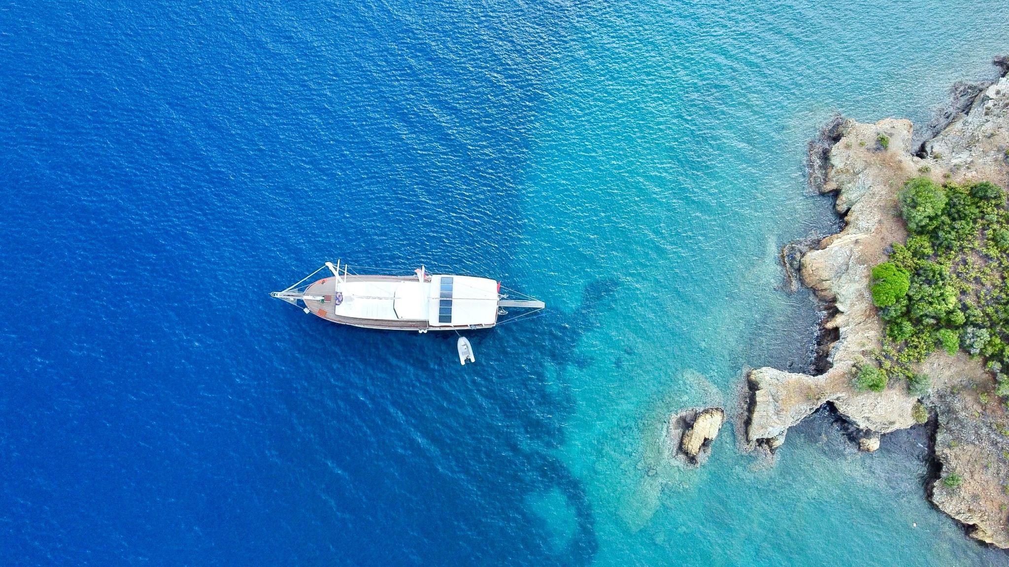 aerial view of white gulet yacht anchored in crystal clear turquoise bay near rocky coastline