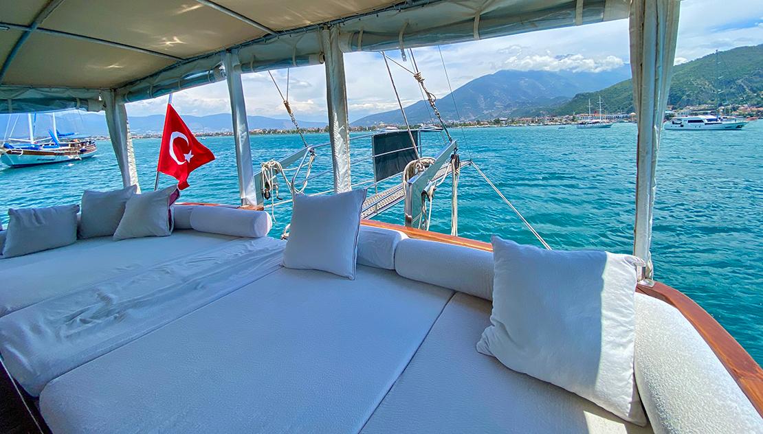 gulet aft deck with white cushioned seating area under canvas awning, Turkish flag visible