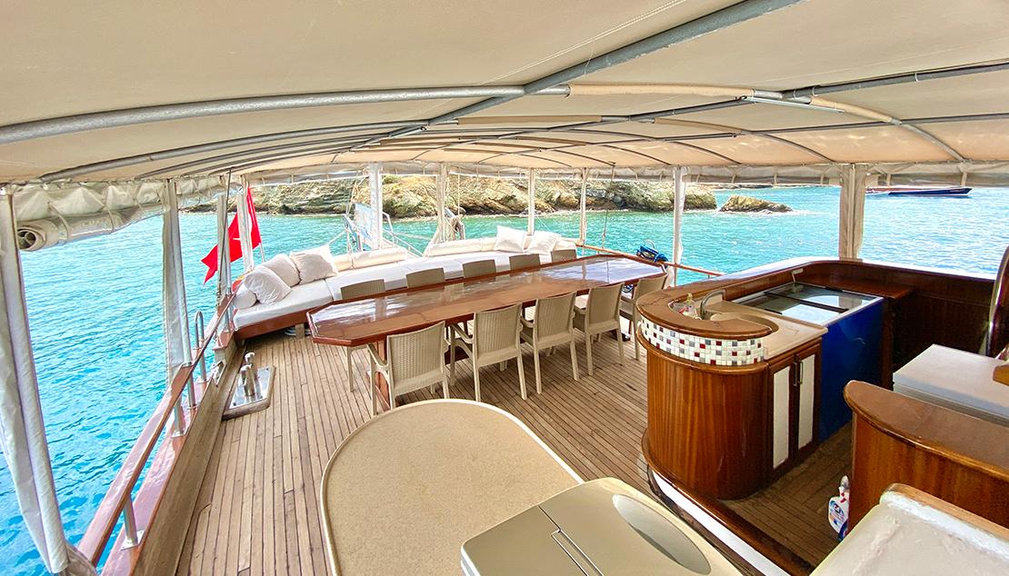 luxury yacht covered aft deck featuring outdoor dining table, curved bar counter, and teak decking