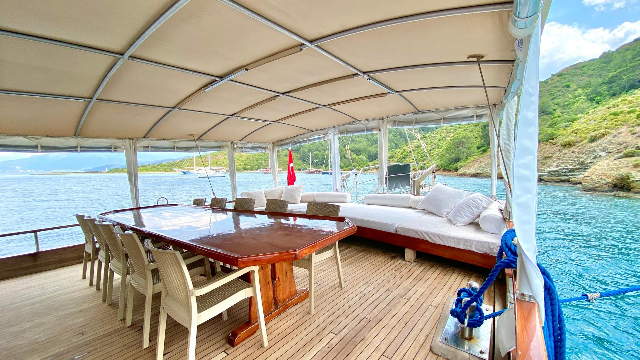 Gulet aft deck with wooden dining table, wicker chairs and daybed under canvas awning