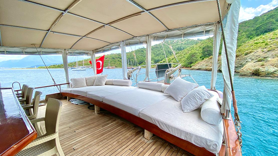 covered aft deck with white daybed seating and cushions overlooking Turkish coastline