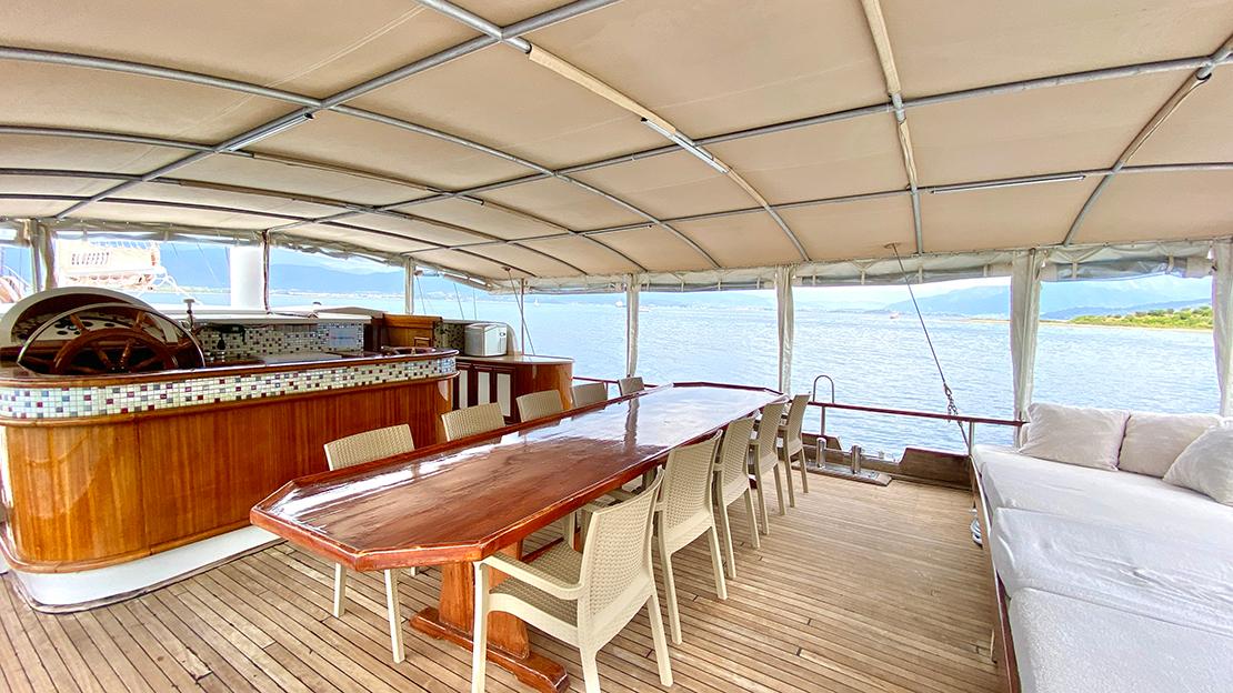 gulet aft deck with wooden dining table, cream chairs and built-in galley bar