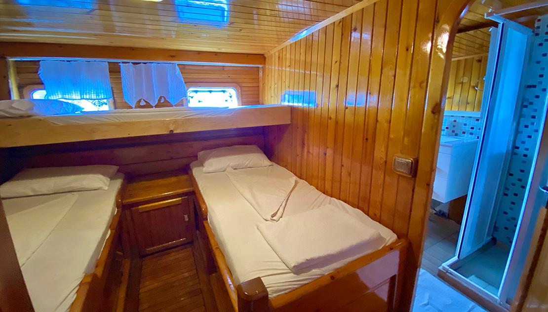 yacht twin cabin with wooden bunk beds, white linens and adjacent ensuite bathroom