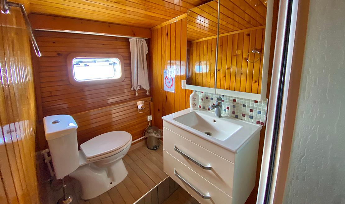 yacht bathroom interior with white toilet, vanity sink, mirror cabinet and round porthole window