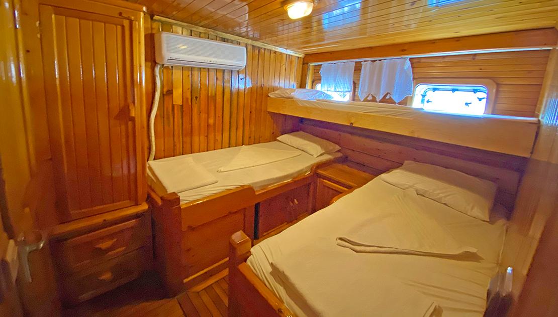 Guest cabin with two single beds, wooden wall paneling, air conditioning unit and porthole window