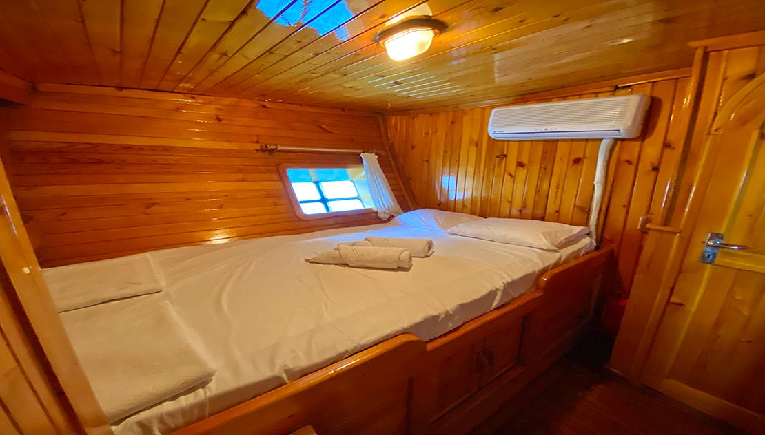 yacht guest cabin with double bed, wooden paneling, porthole window and air conditioning