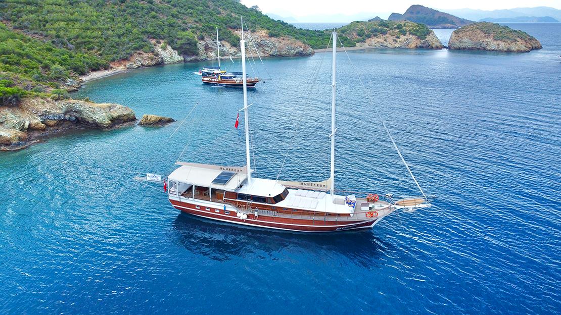 aerial view of traditional wooden gulet yacht anchored in turquoise Mediterranean bay with rocky coastline