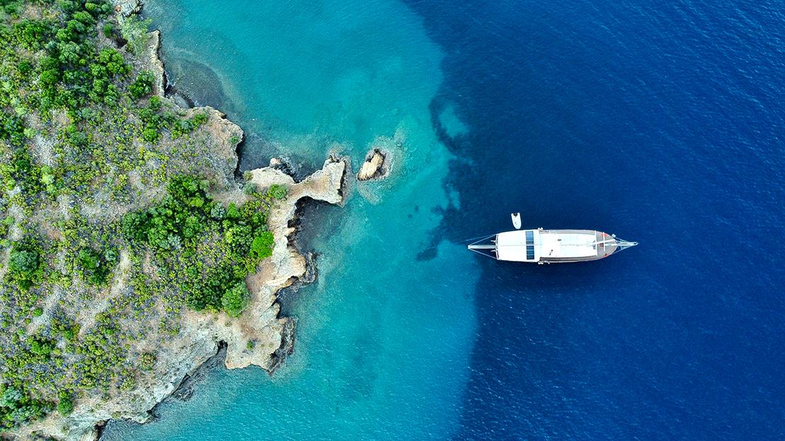 aerial view of white luxury yacht anchored in crystal clear turquoise waters near Mediterranean coastline