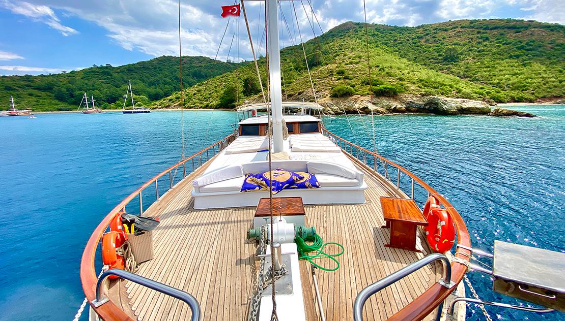 Traditional gulet forward deck with white cushioned sunbathing area and central mast at anchor
