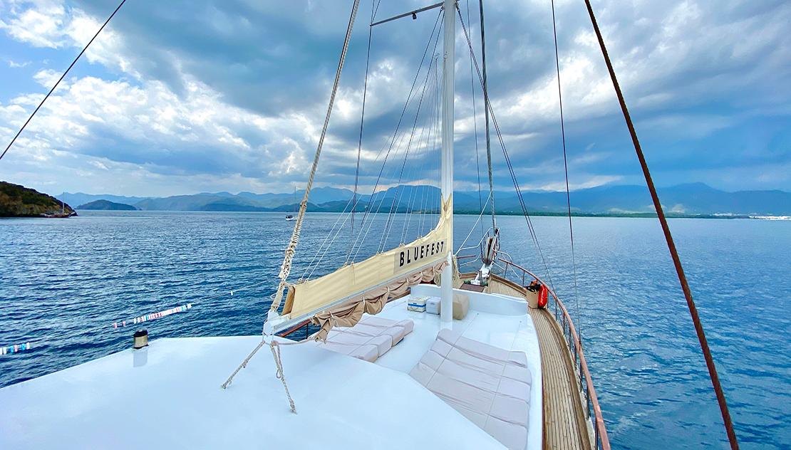 gulet bow deck with white cushioned seating area and rigging against blue sky