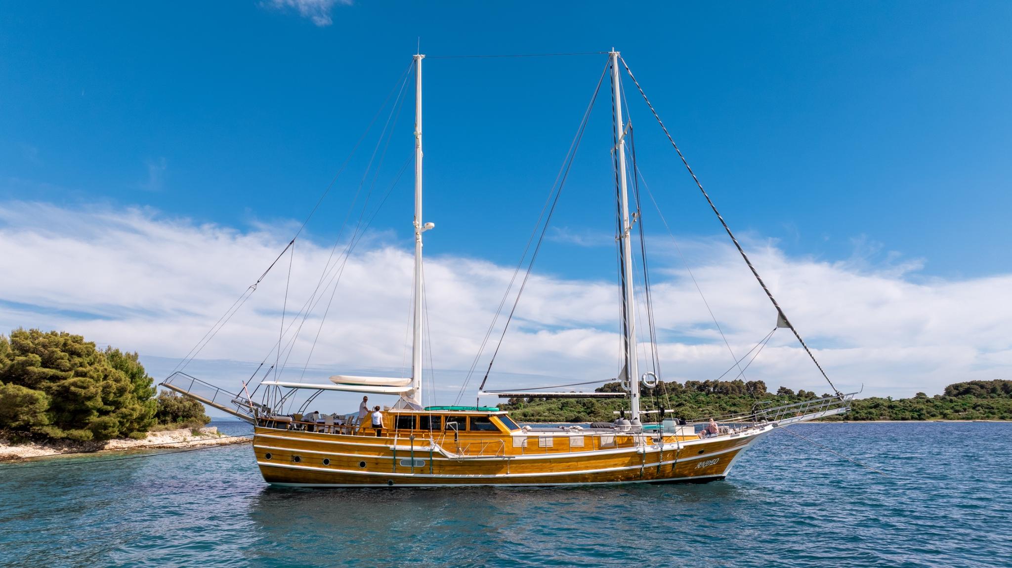 Traditional wooden gulet with two masts anchored in turquoise waters near green coastline