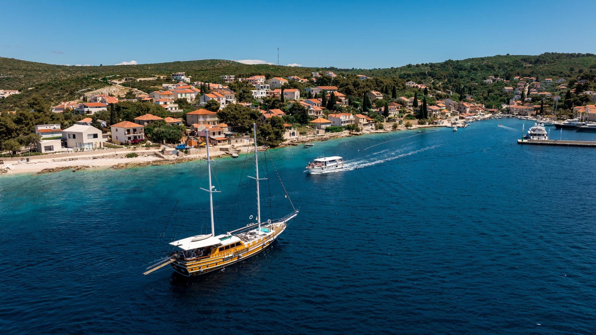 aerial view of traditional wooden gulet yacht anchored in turquoise bay near coastal village