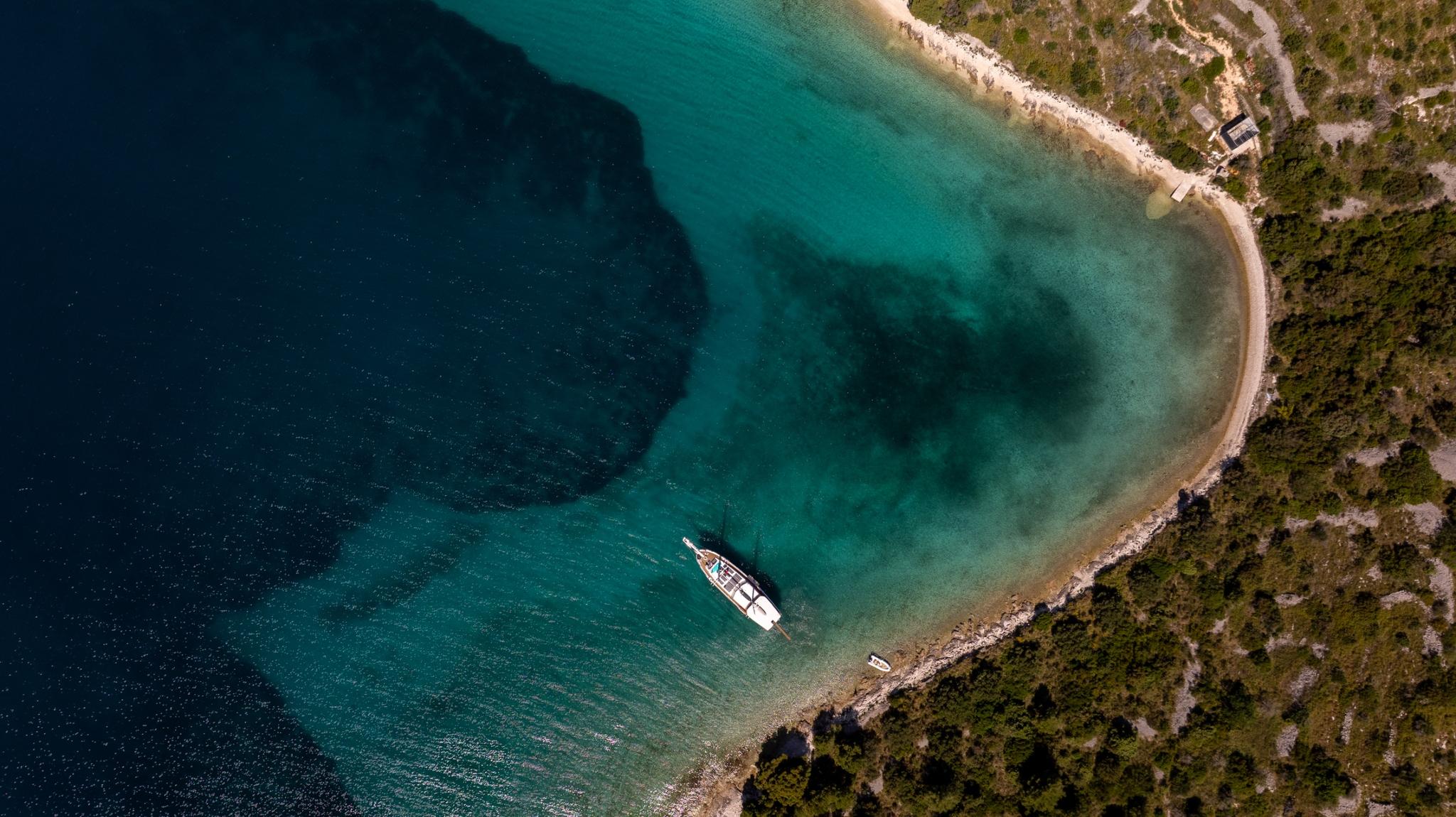 aerial view of white yacht anchored in secluded turquoise bay with rocky coastline