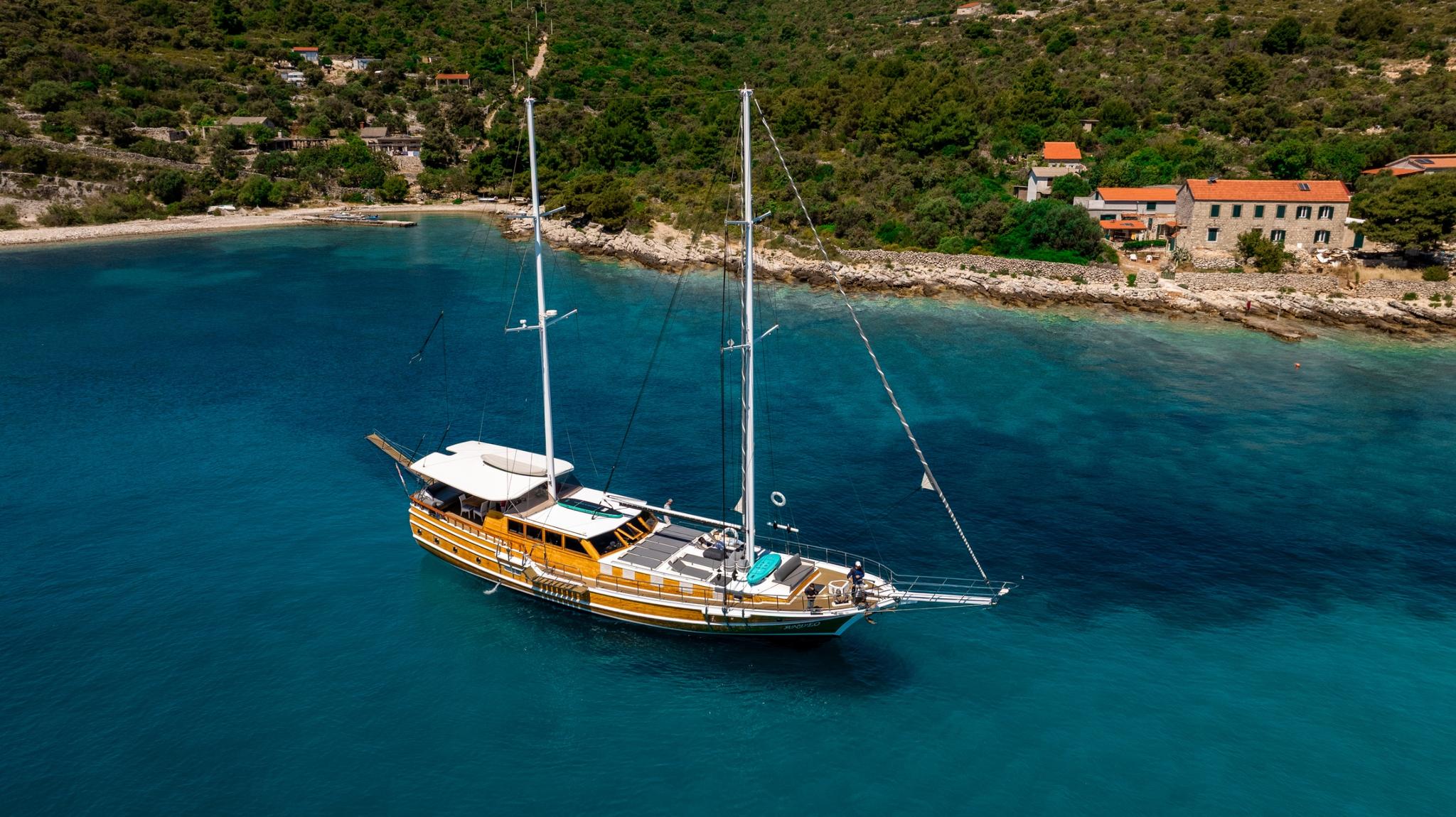 aerial view of traditional wooden gulet yacht anchored in crystal clear turquoise waters near Mediterranean coastline