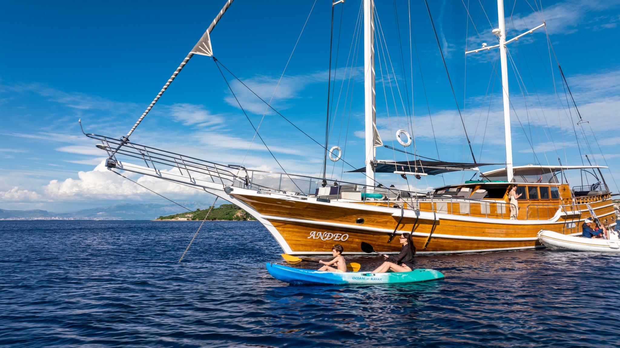 two guests kayaking in blue waters next to wooden gulet ANDEO at anchor