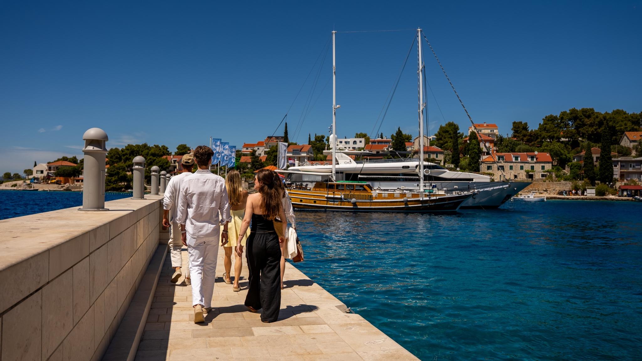 Traditional wooden gulet yacht moored in crystal blue Mediterranean harbor with guests walking stone pier