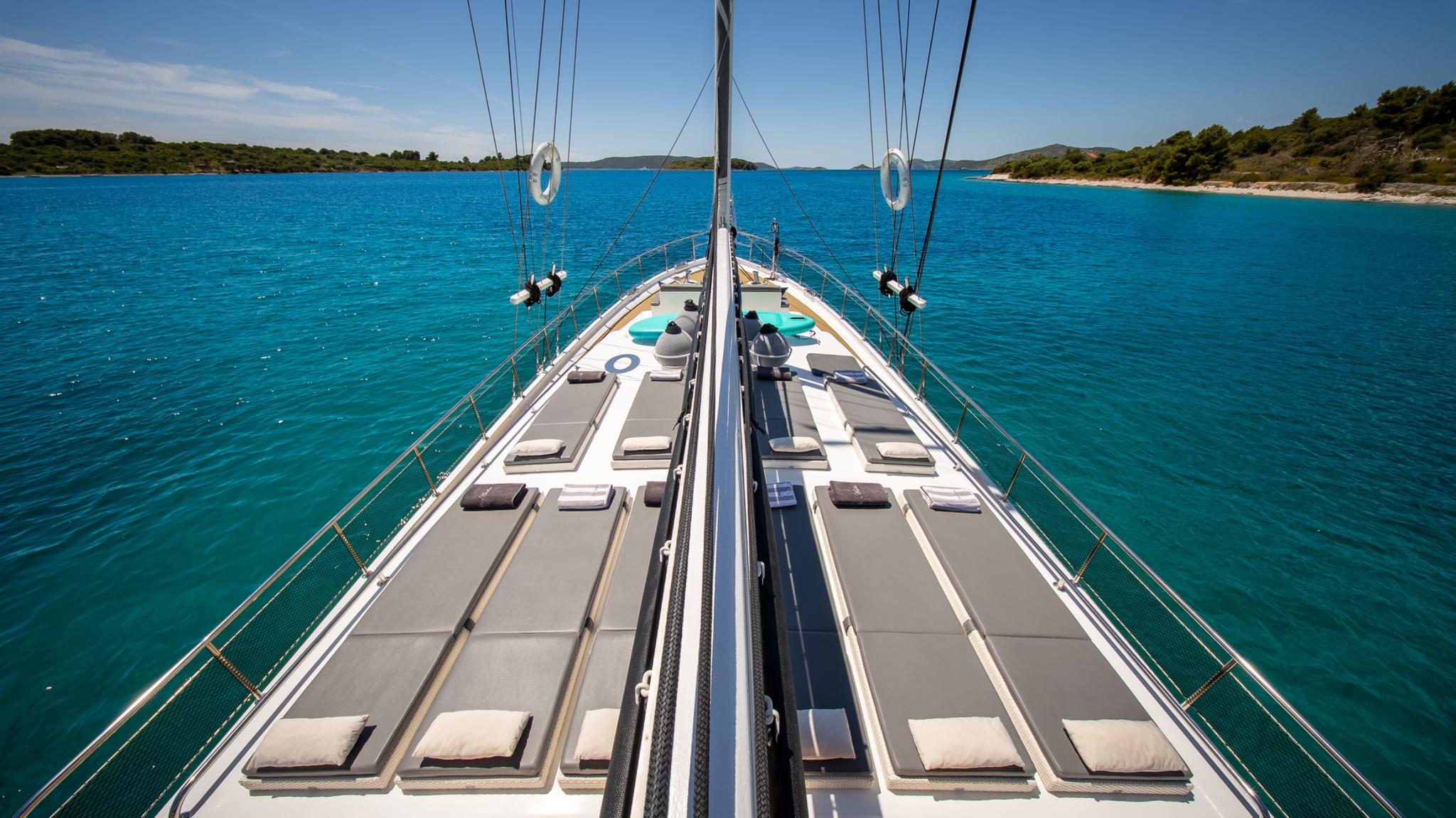 bow sun deck with gray cushioned loungers and circular jacuzzi in turquoise waters