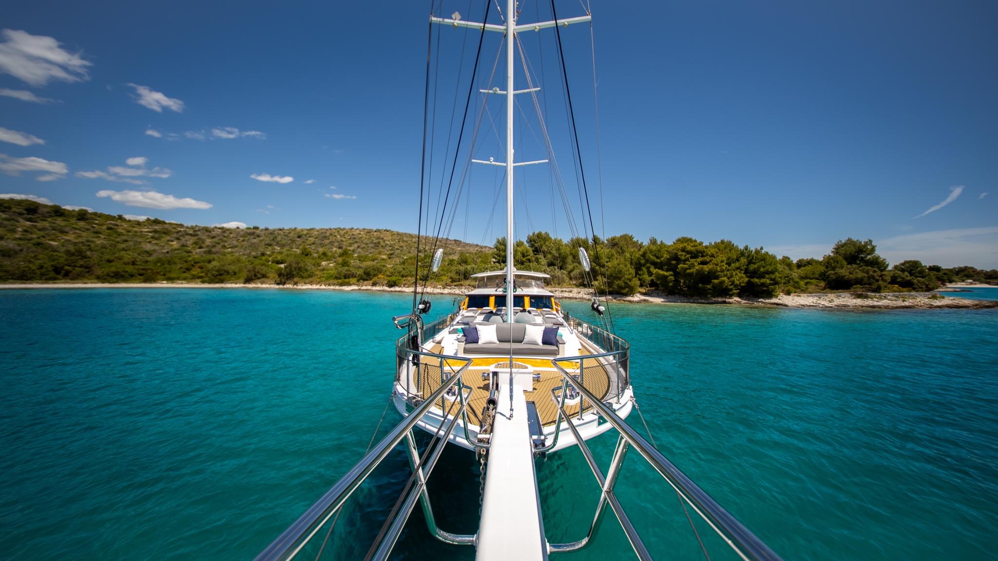 white gulet bow deck with cushioned seating area anchored in turquoise bay