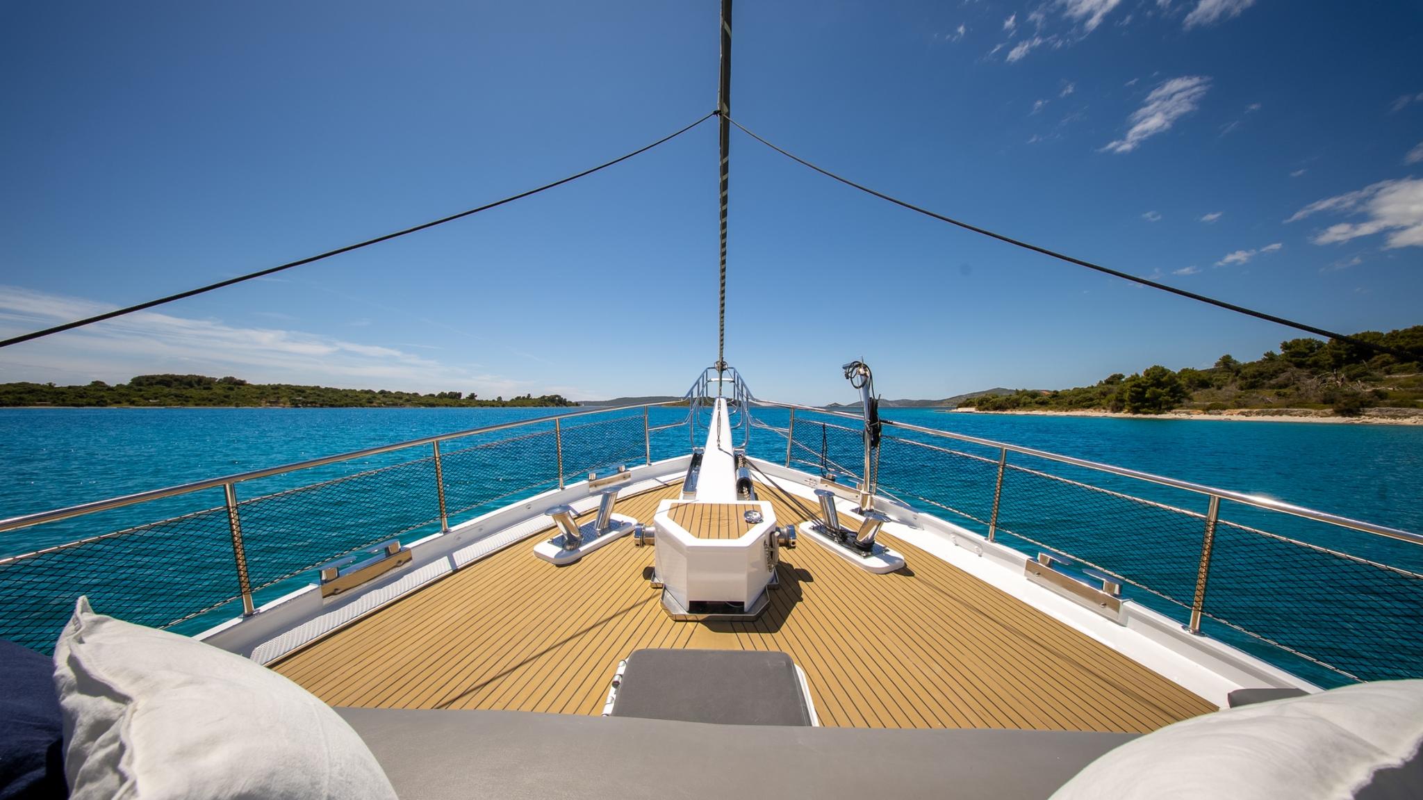 Yacht bow deck featuring teak decking, white safety netting, and anchor windlass in turquoise waters