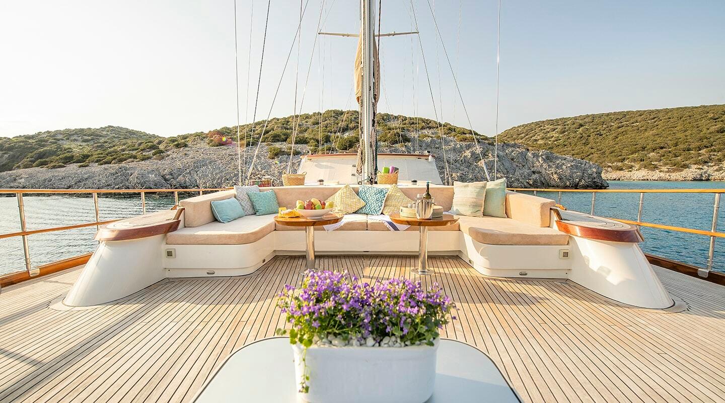 gulet aft deck with built-in seating, teak decking, central mast and rigging overlooking Mediterranean coastline