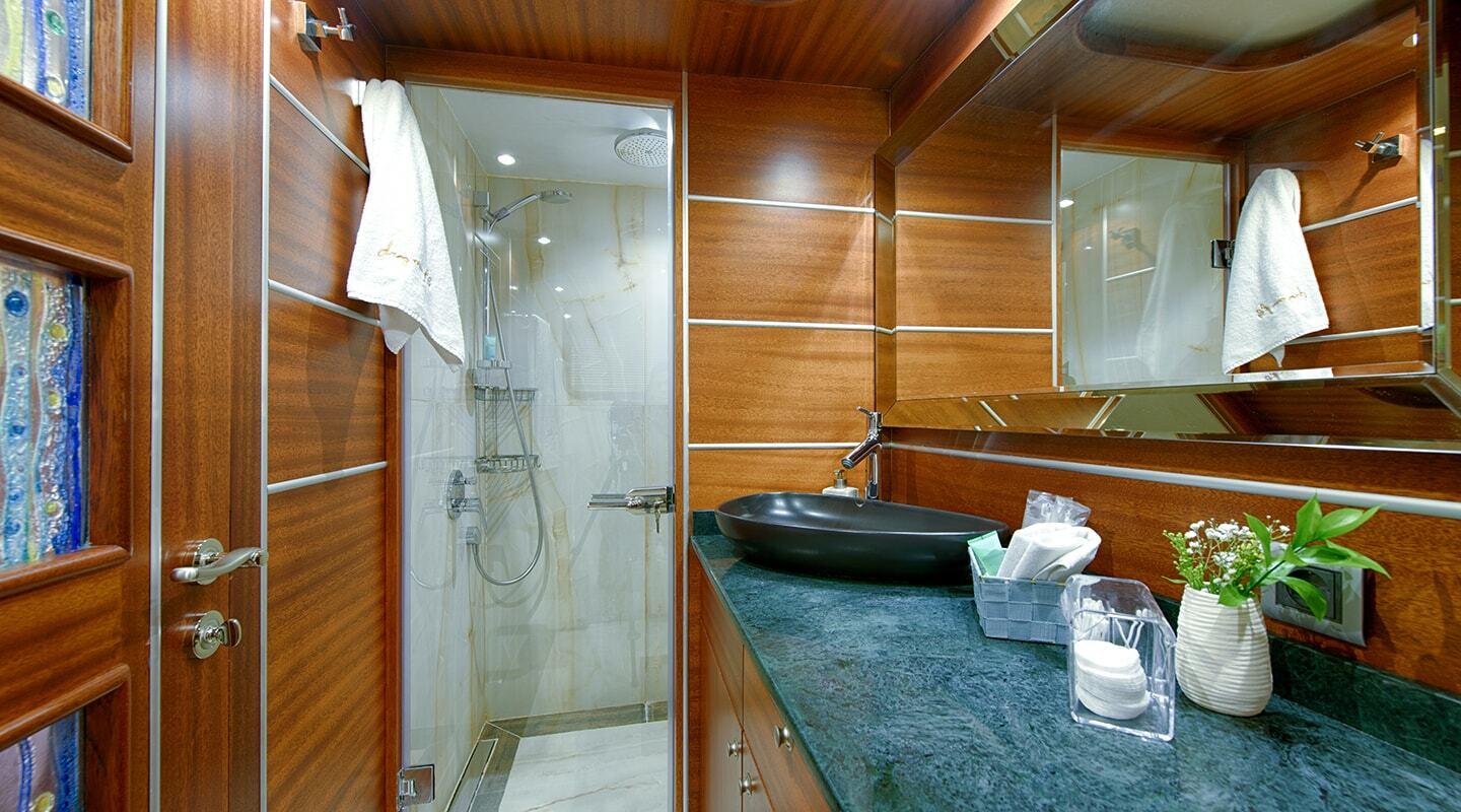 luxury yacht bathroom featuring glass shower enclosure, dark stone vessel basin, and warm wood paneling