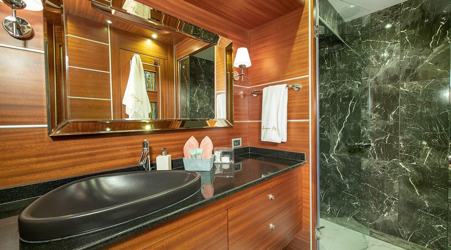 luxury yacht bathroom featuring black marble shower walls and wooden vanity with oval basin