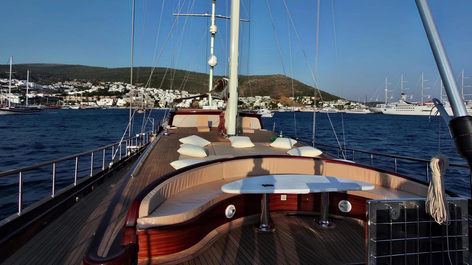 gulet aft deck with curved bench seating around white round table, teak decking