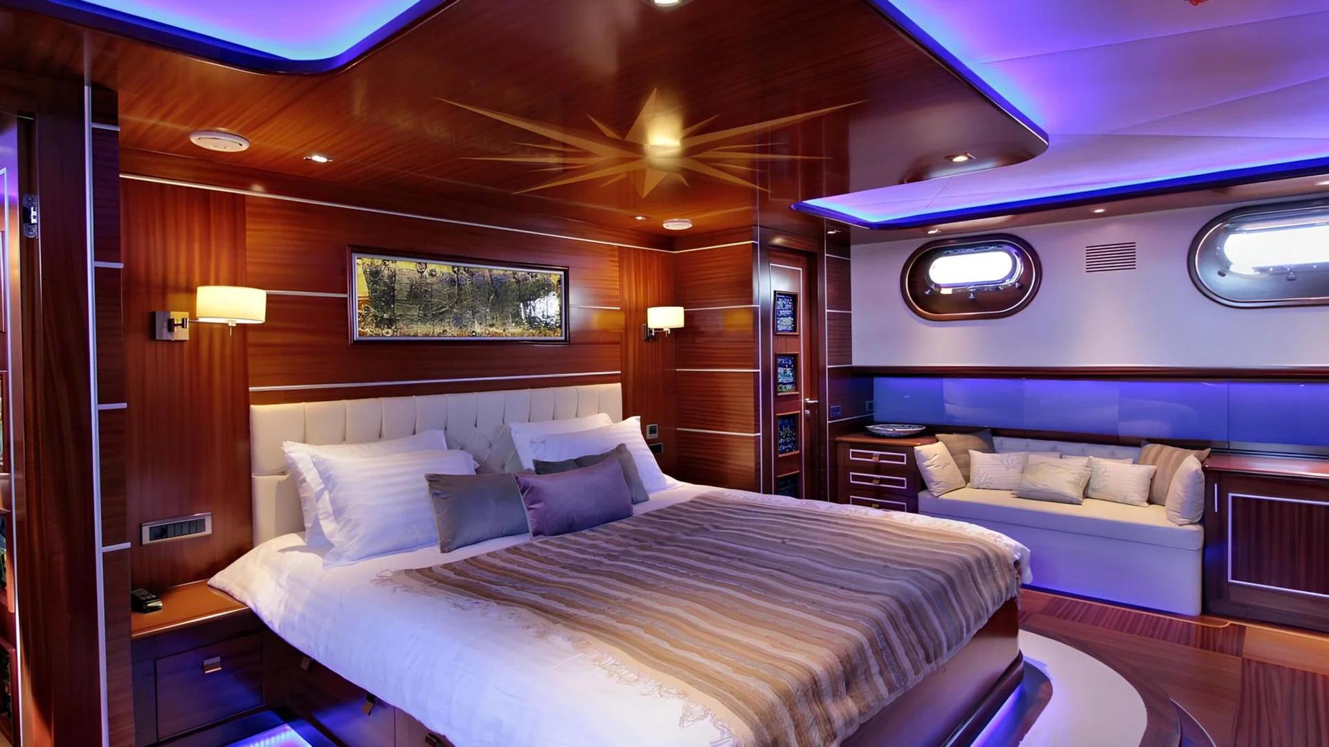 Master cabin interior featuring king bed, tufted headboard, wood paneling and oval portholes