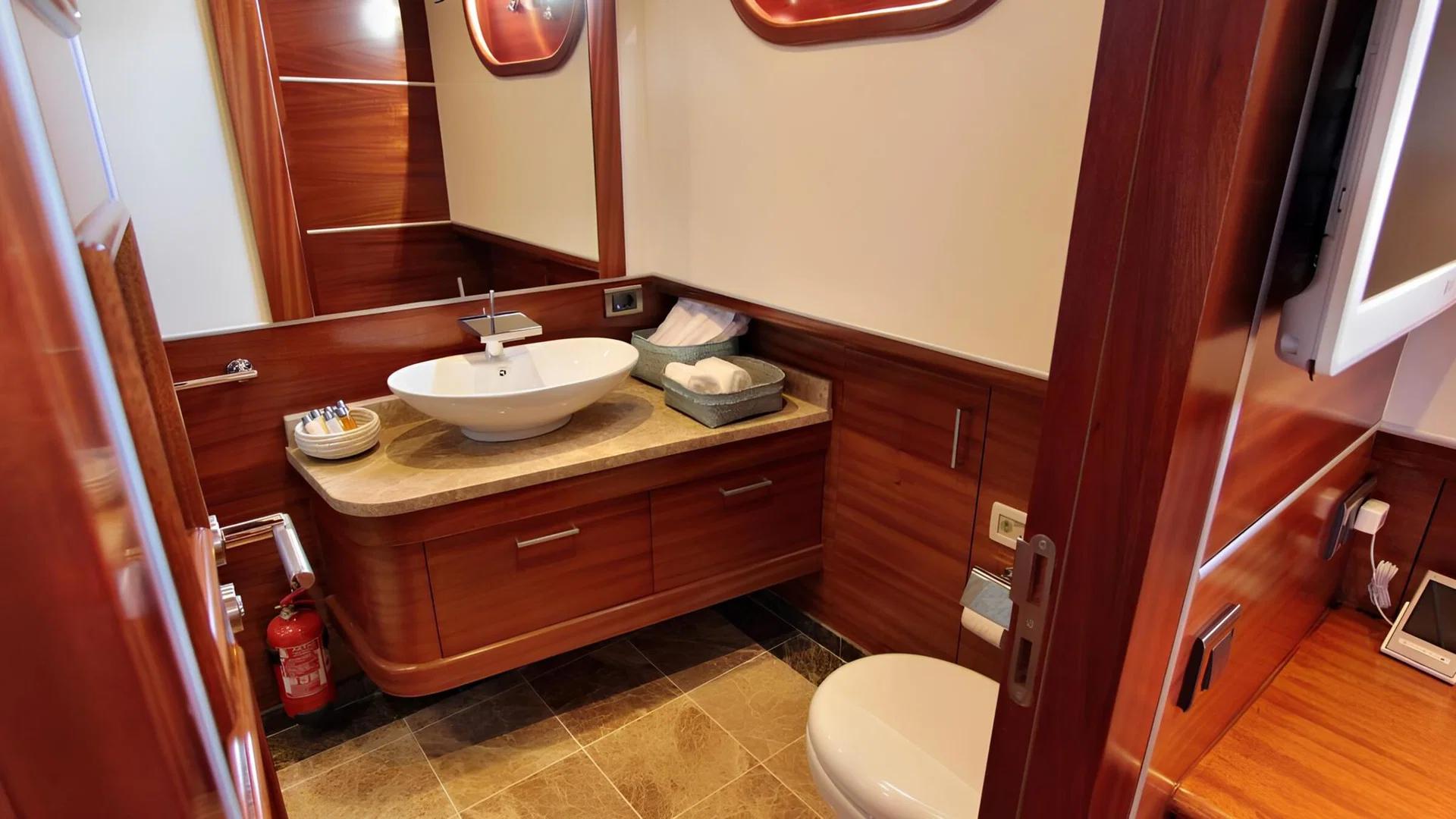 yacht bathroom featuring oval vessel sink on marble countertop with toilet and rich wood paneling