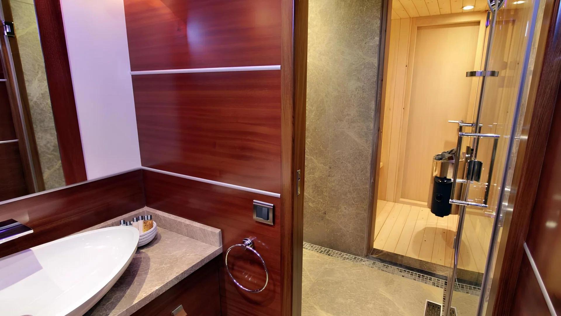 luxury yacht sauna with wooden interior and glass door next to marble bathroom