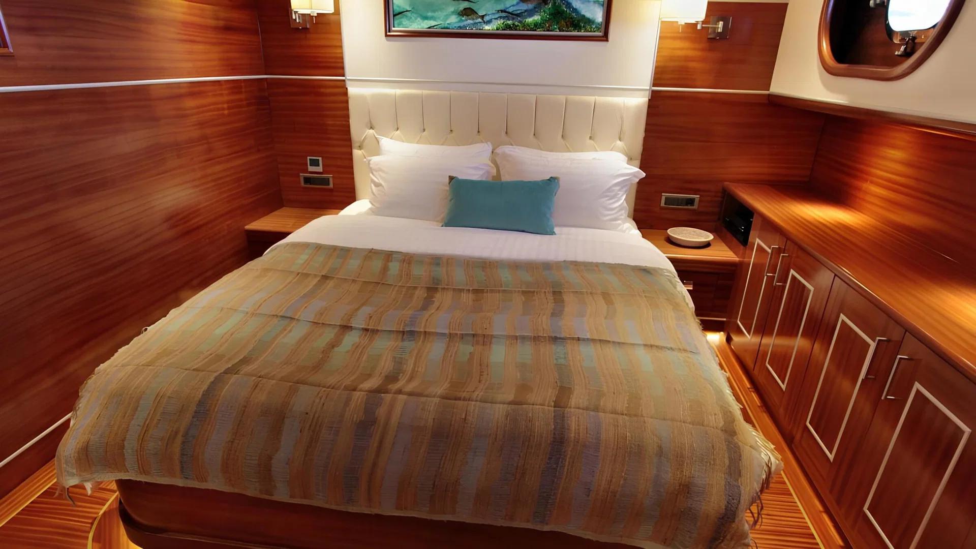 yacht guest cabin featuring double bed with striped throw, white leather headboard and rich wood paneling
