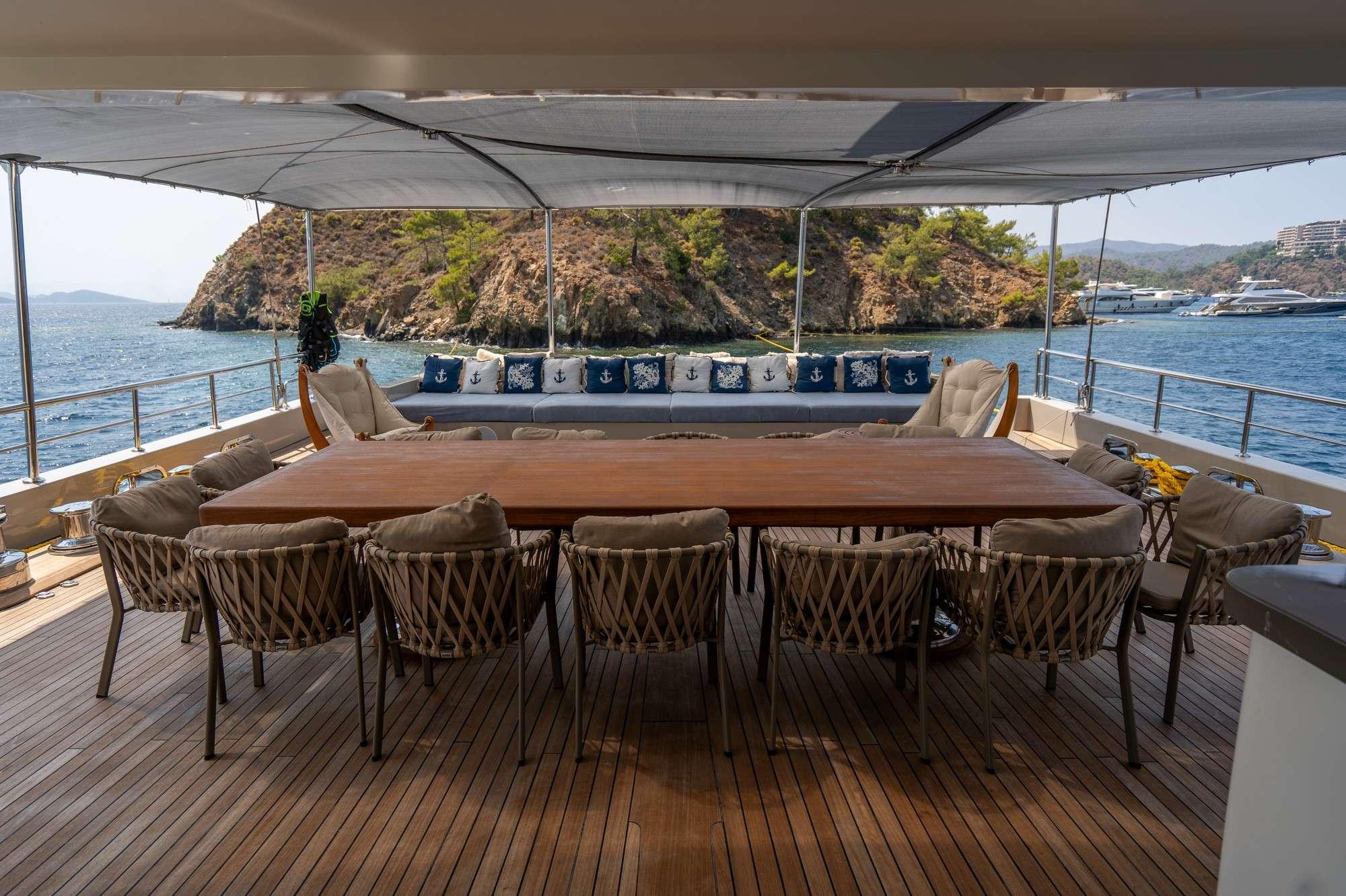 yacht aft deck featuring teak dining table with woven chairs under canopy awning