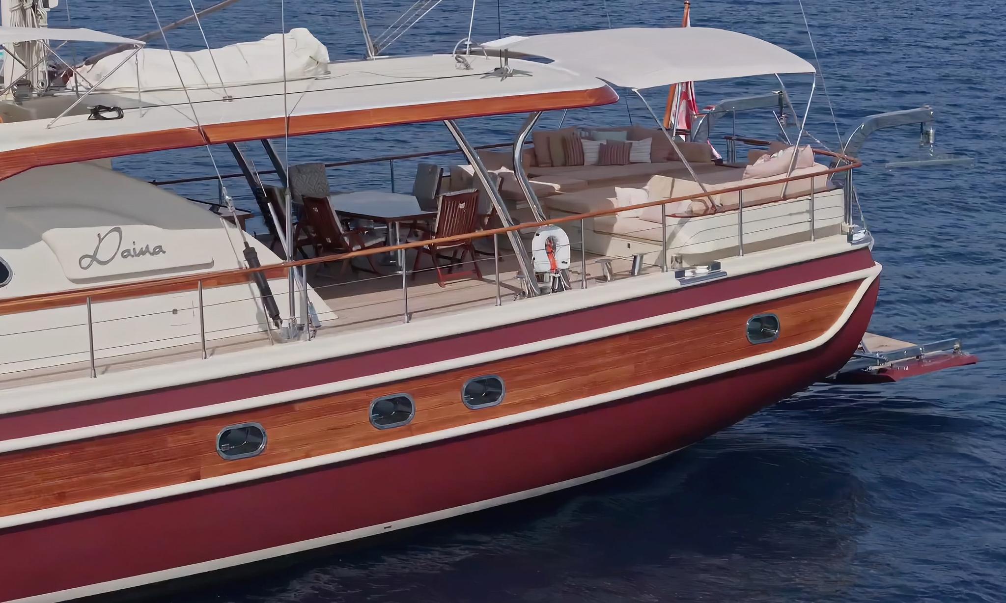 Traditional gulet yacht named Laura showing wooden hull with red stripe and aft deck dining area