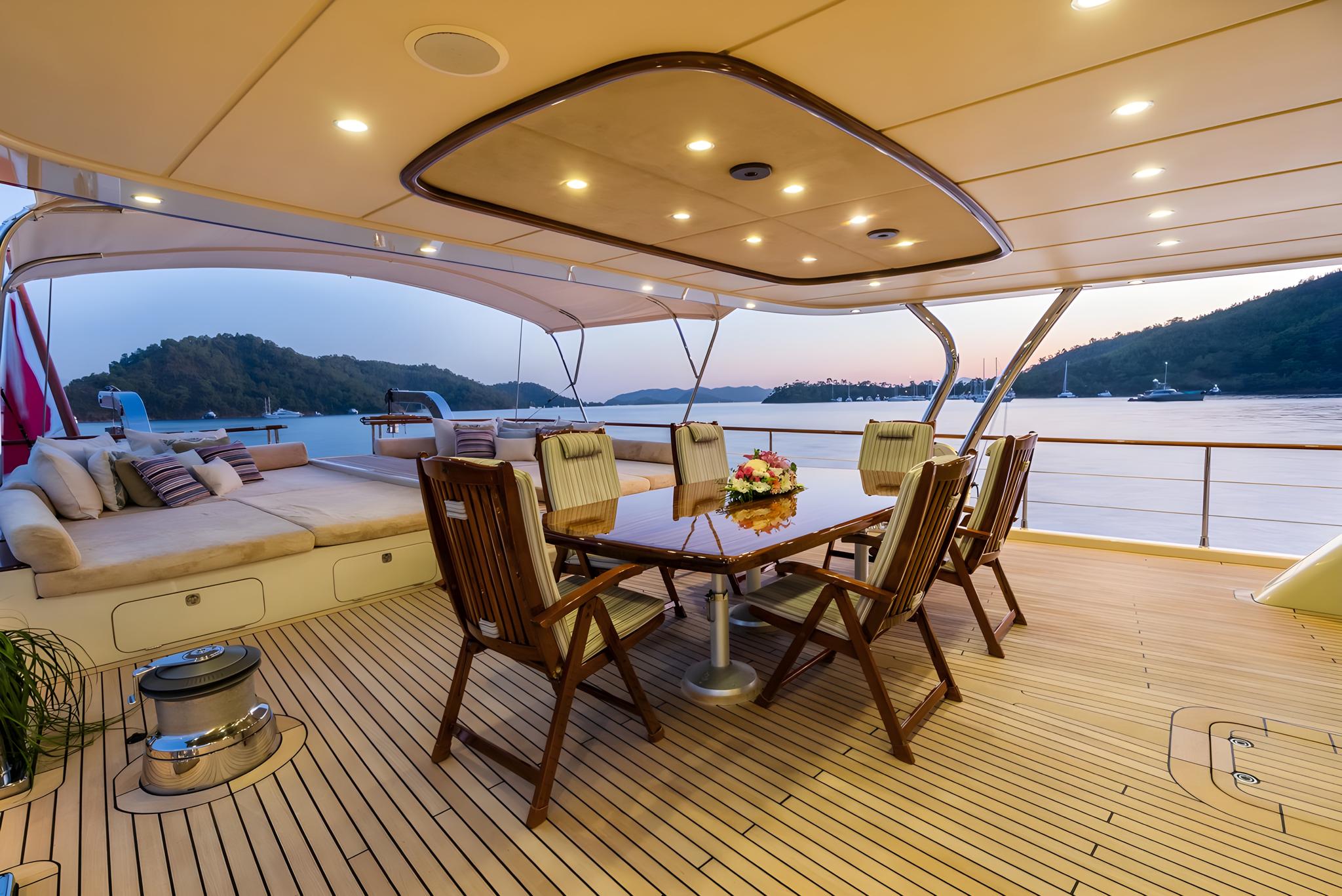 aft deck dining area with teak table, folding chairs and built-in seating under hardtop