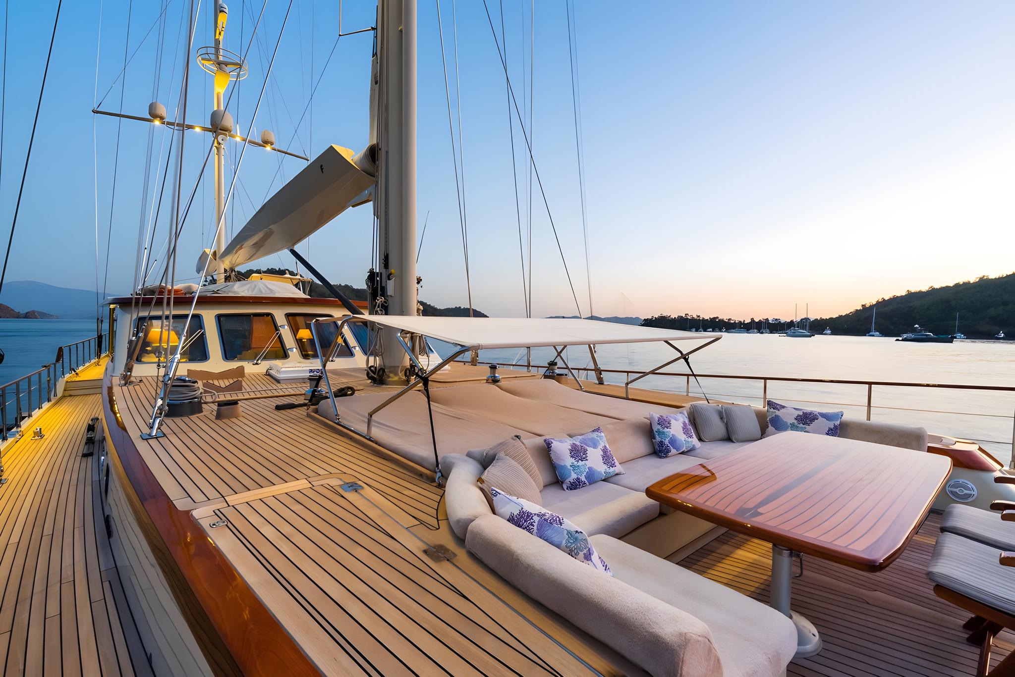 gulet main deck with curved seating, wooden dining table and rigging at sunset