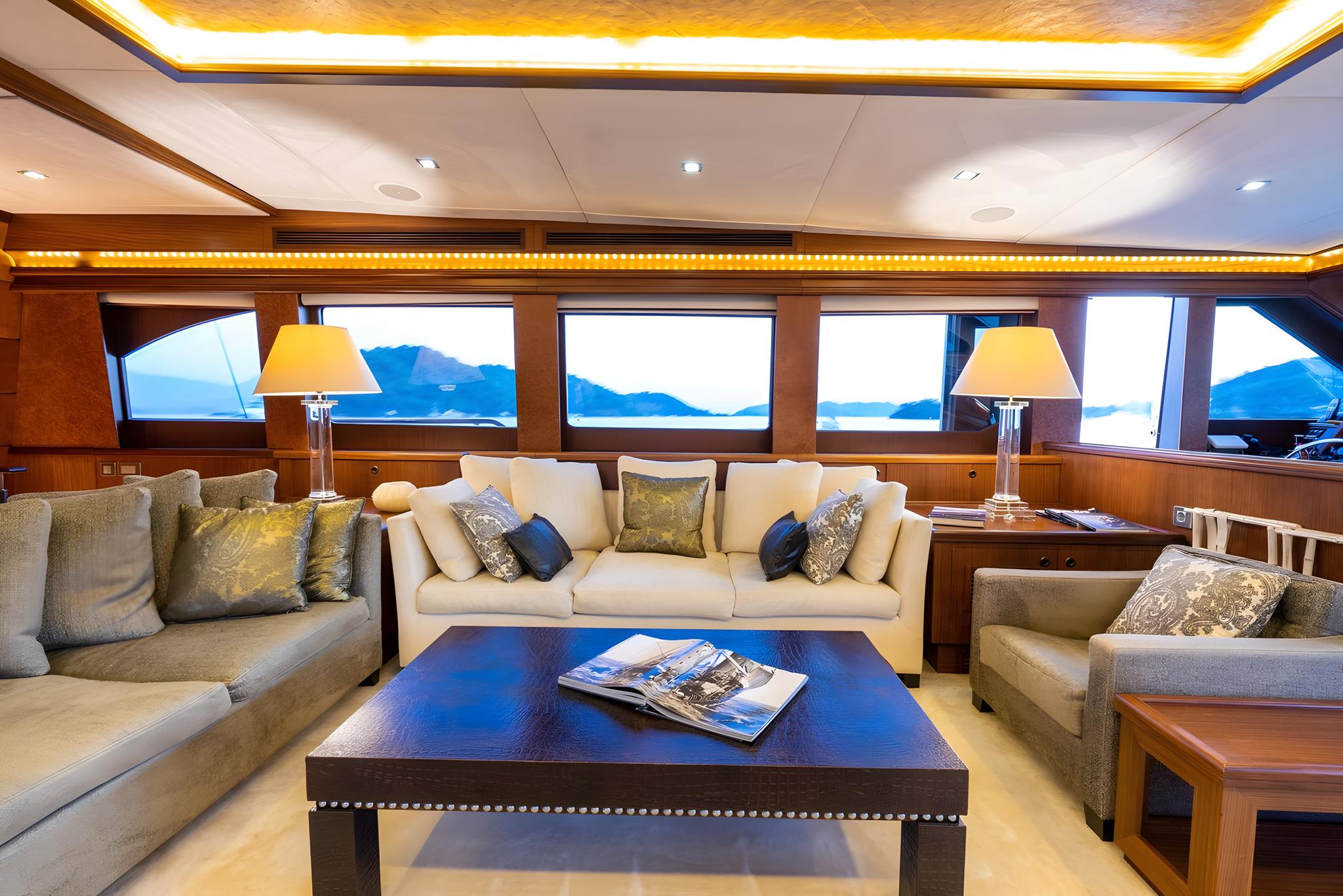 luxury yacht main salon with wraparound seating, coffee table and panoramic side windows showing coastline