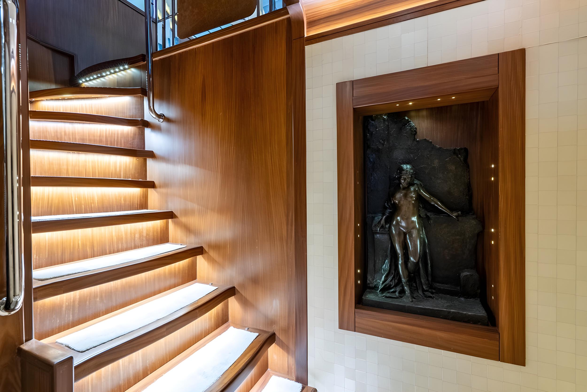 yacht interior staircase with LED lighting and bronze sculpture in wooden display niche