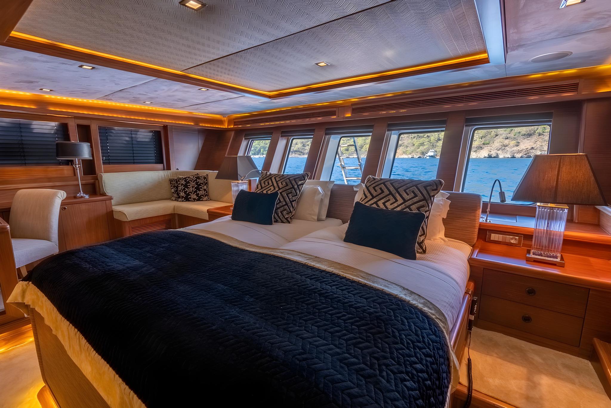 Master cabin interior with king bed, panoramic side windows, wood paneling and cream upholstery