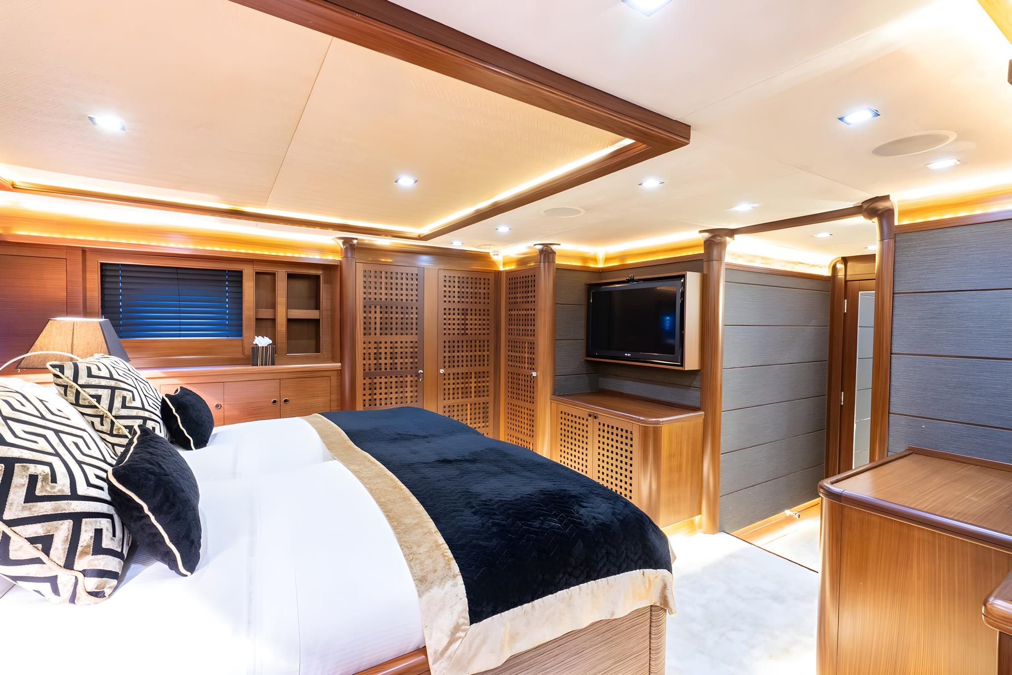 luxury yacht master cabin featuring king bed with navy throw, wall-mounted television, and warm wood paneling