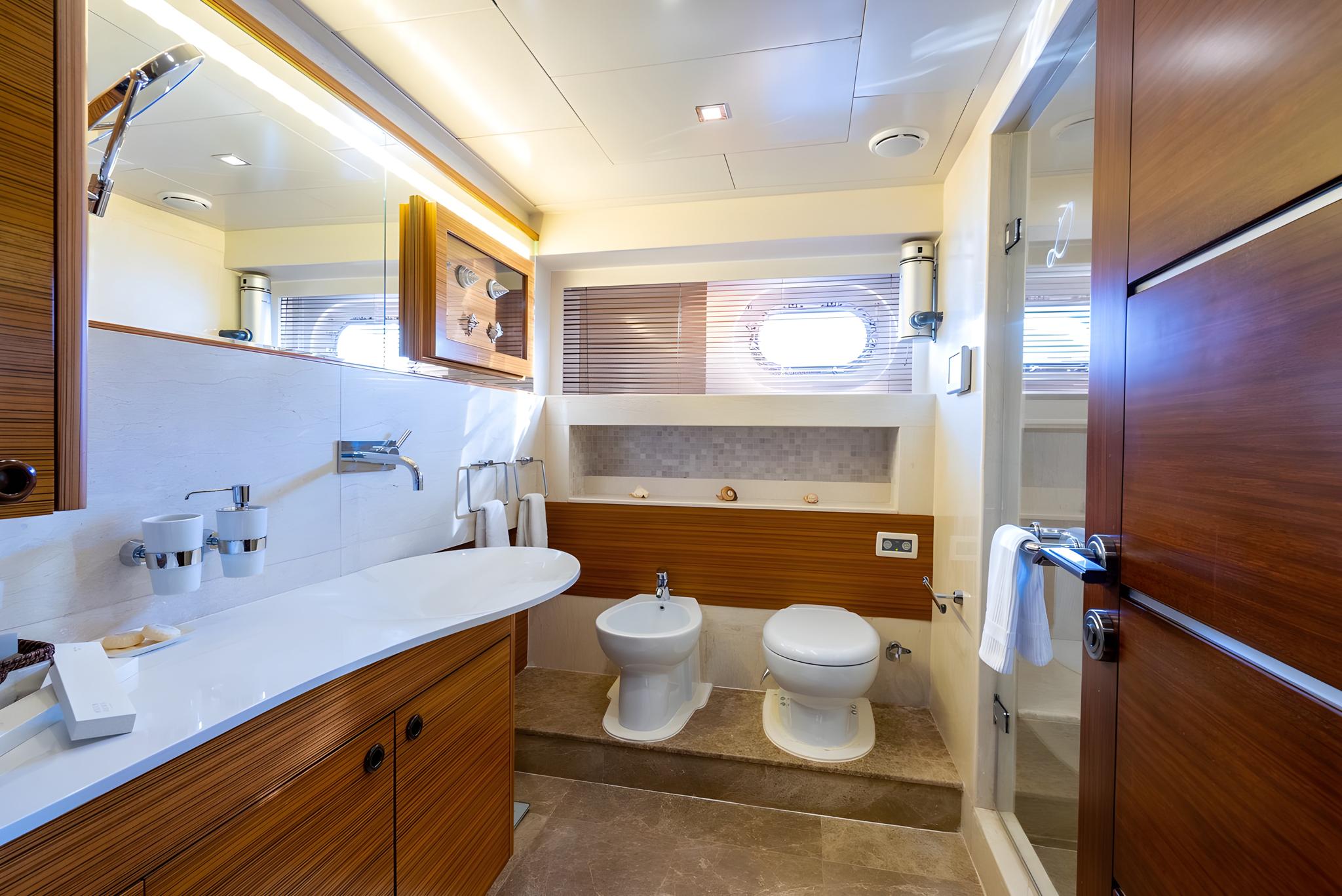 luxury yacht bathroom featuring built-in bathtub, vessel sink, bidet, toilet and teak wood finishes