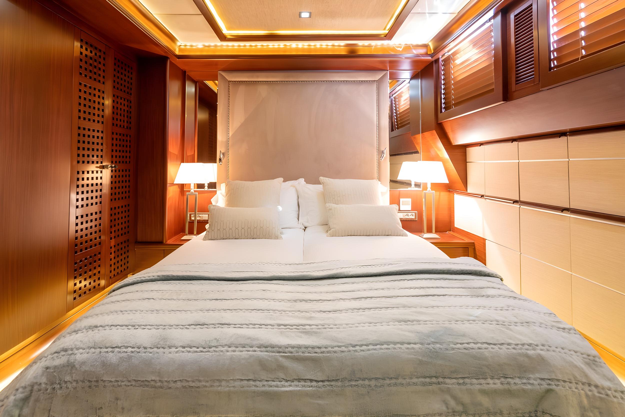 luxury yacht master cabin featuring king bed with upholstered headboard and warm wood paneling