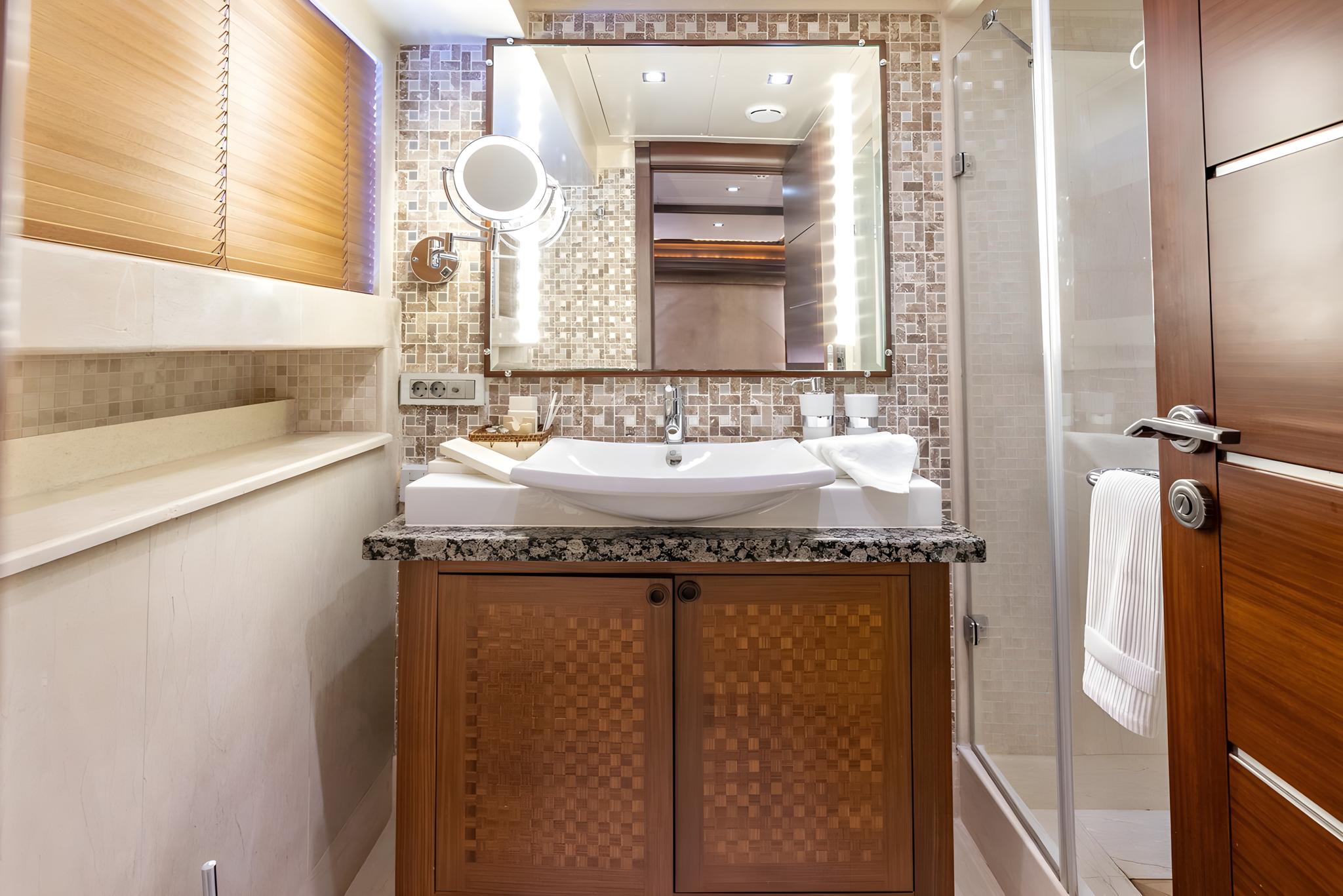 luxury yacht bathroom featuring mosaic tile walls, granite countertop with white vessel sink, and illuminated mirror