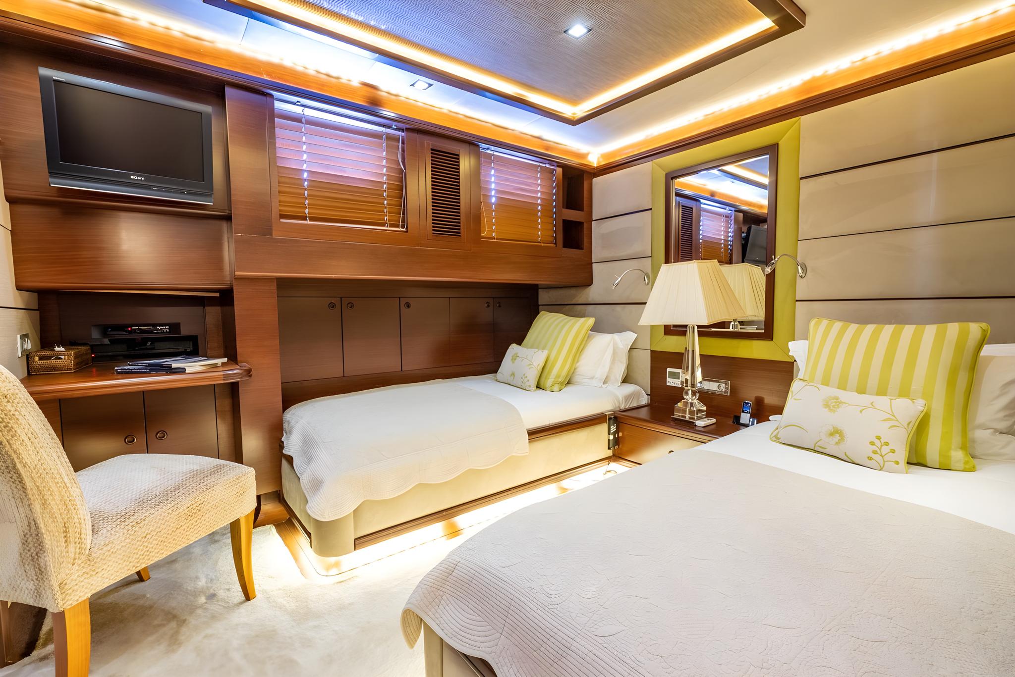 luxury yacht guest cabin with two single beds, wall-mounted TV, wooden paneling and portholes