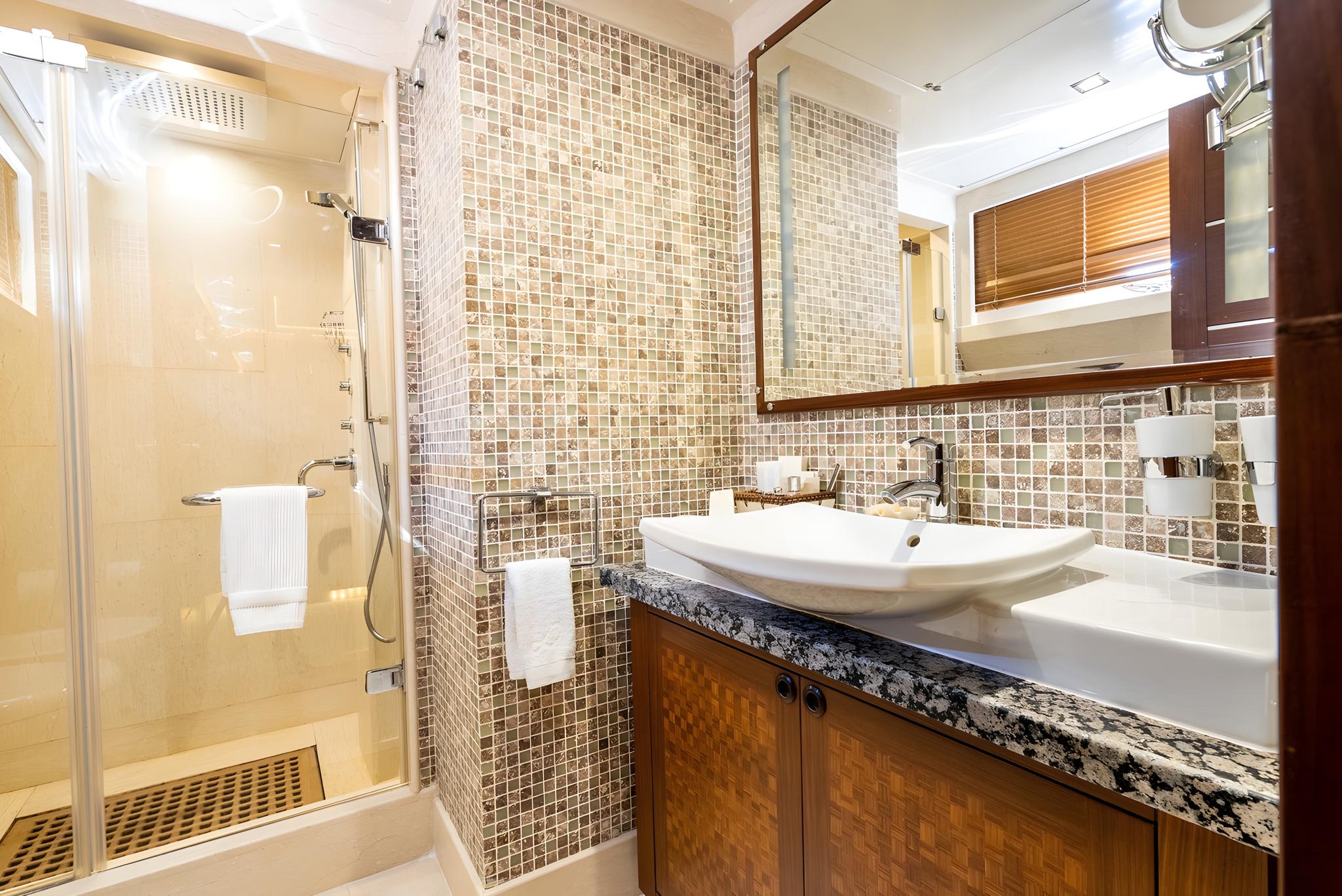 yacht bathroom featuring mosaic tile walls, white vessel sink on granite countertop and glass shower