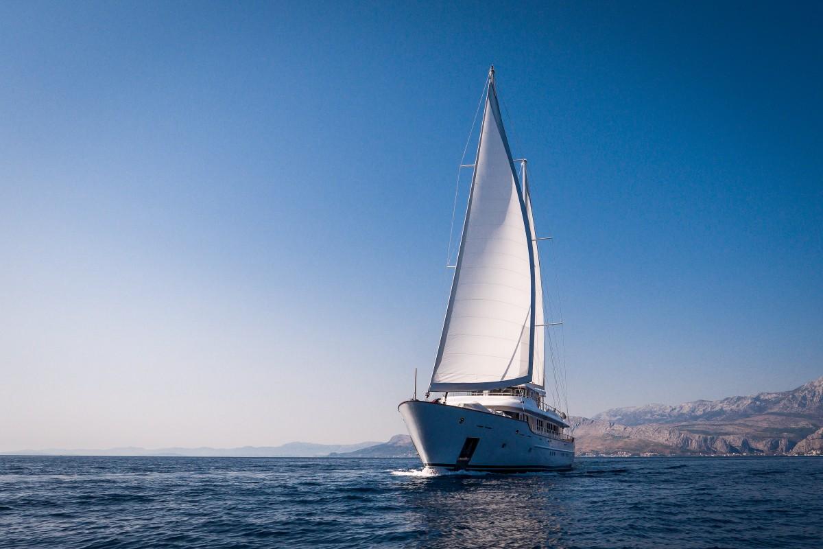 Large white sailing yacht with deployed sails cruising on calm blue Mediterranean waters