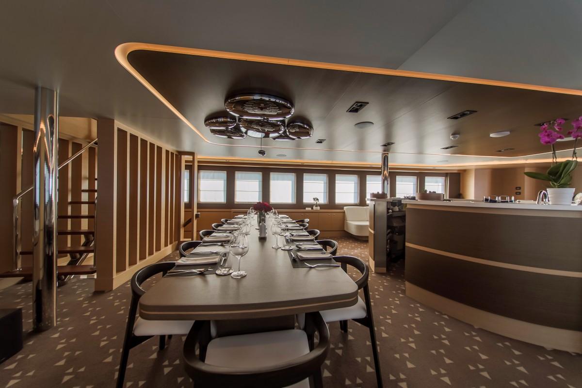 Modern yacht interior dining salon with formal table seating and galley kitchen