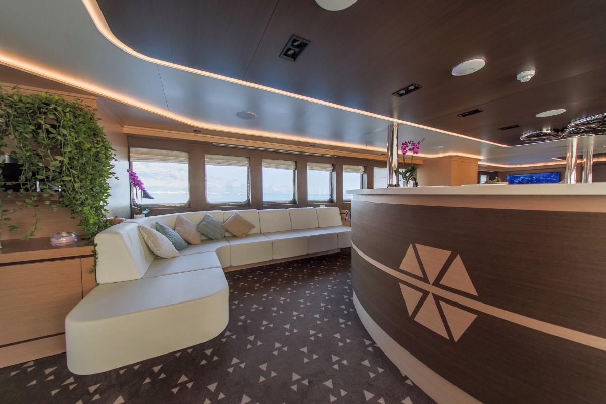 Modern yacht main salon featuring curved white leather seating and compass rose bar