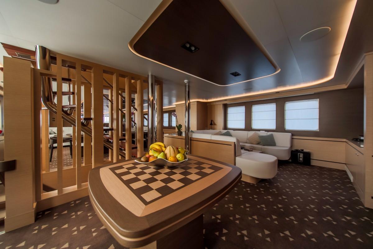 Yacht main salon featuring curved chess table and cream banquette seating