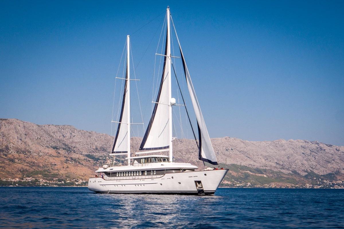 luxury white sailing yacht with two masts sailing near rocky coastline