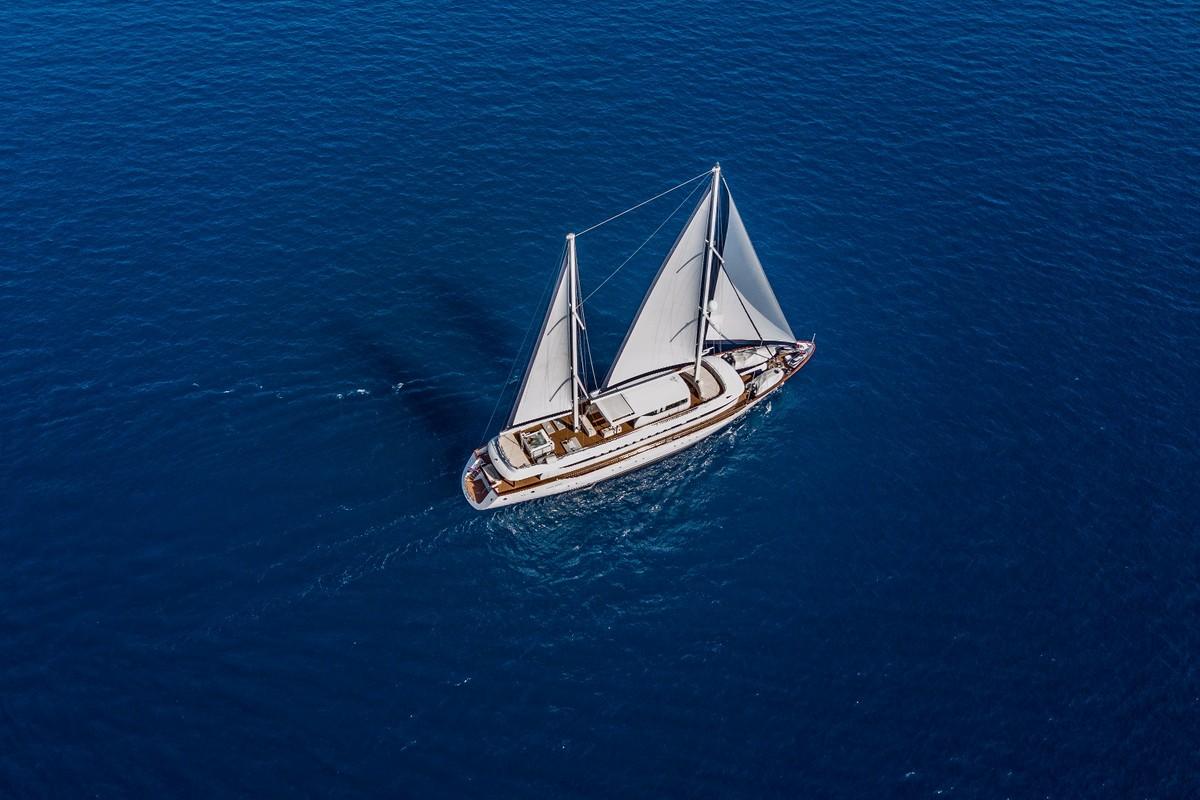 Aerial view of traditional wooden gulet with white sails on blue water